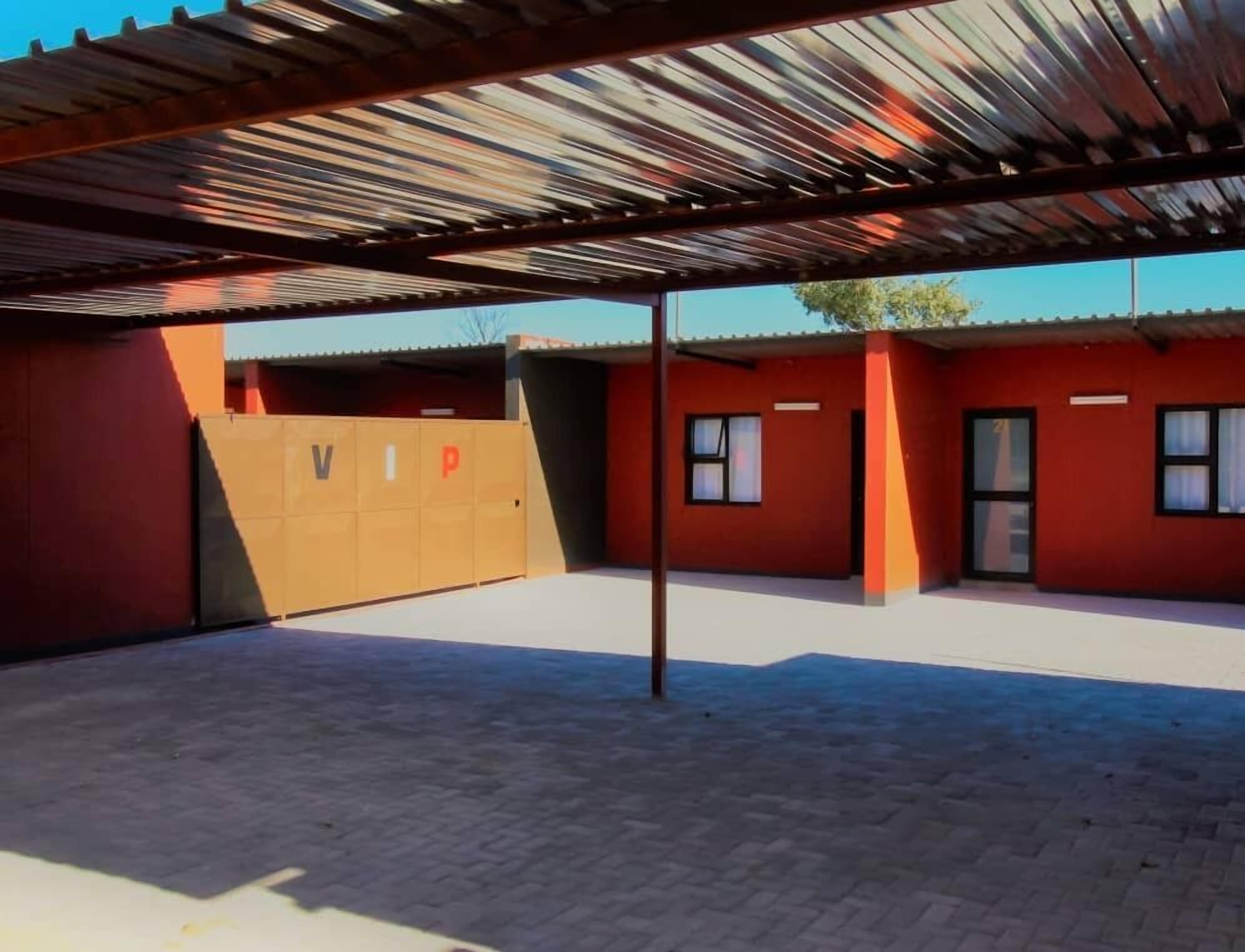 A covered outdoor area with a red building, a wooden gate with letters, and a paved floor.