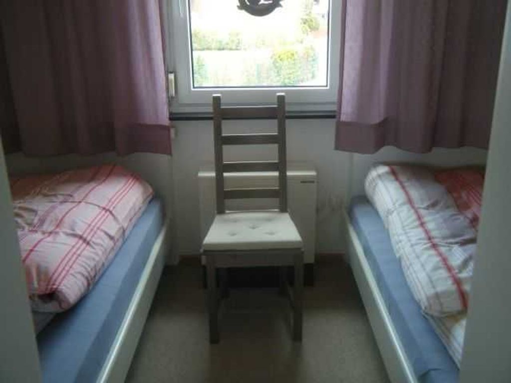 Une petite pièce avec deux lits, une chaise et une fenêtre.