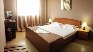 Une chambre d’hôtel avec un grand lit, deux tables de chevet avec des lampes, un petit bureau avec un ordinateur et une fenêtre avec des rideaux.