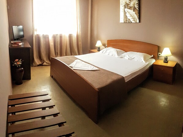 Habitación de hotel con una cama grande, dos mesitas de noche con lámparas, un escritorio pequeño con una computadora y una ventana con cortinas.