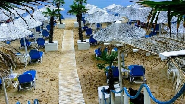 Une plage bordée de rangées de chaises bleues et d’ombrelles en chaume, qui s’étend jusqu’à l’océan.