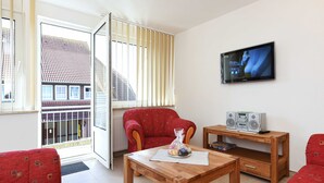 A living room with a wooden table, red sofa, and a television mounted on the wall.