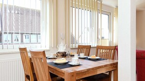 A dining area with a wooden table and chairs, a window with blinds, and a radiator.