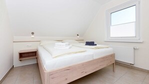 A bedroom with a wooden bed, a nightstand, a window with blinds, and a radiator.