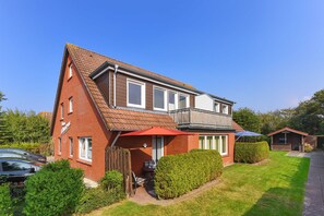 Une maison à deux étages avec une façade en briques rouges, un balcon et un parasol rouge.