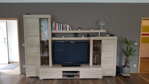 A modern entertainment unit with a flat-screen TV, built-in shelves, and decorative items. - Apartment in Fürstenwalde (Fürstenwalde/Spree)