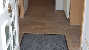 A hallway with a tiled floor, a doormat, a radiator, and a door with a brass handle. - Apartment in Fürstenwalde (Fürstenwalde/Spree)