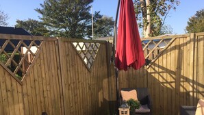 Eine Holzterrasse mit Korbmöbeln, einem Tisch und einem roten Sonnenschirm.