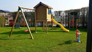 Ein Spielplatz mit Schaukel, Rutsche und einer kleinen Holzkonstruktion.