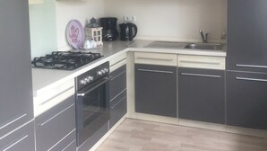 Eine moderne Küche mit schwarzen Schränken, einer weißen Arbeitsplatte, einem Gasherd, einem Backofen, einem Spülbecken und einer Kaffeemaschine.