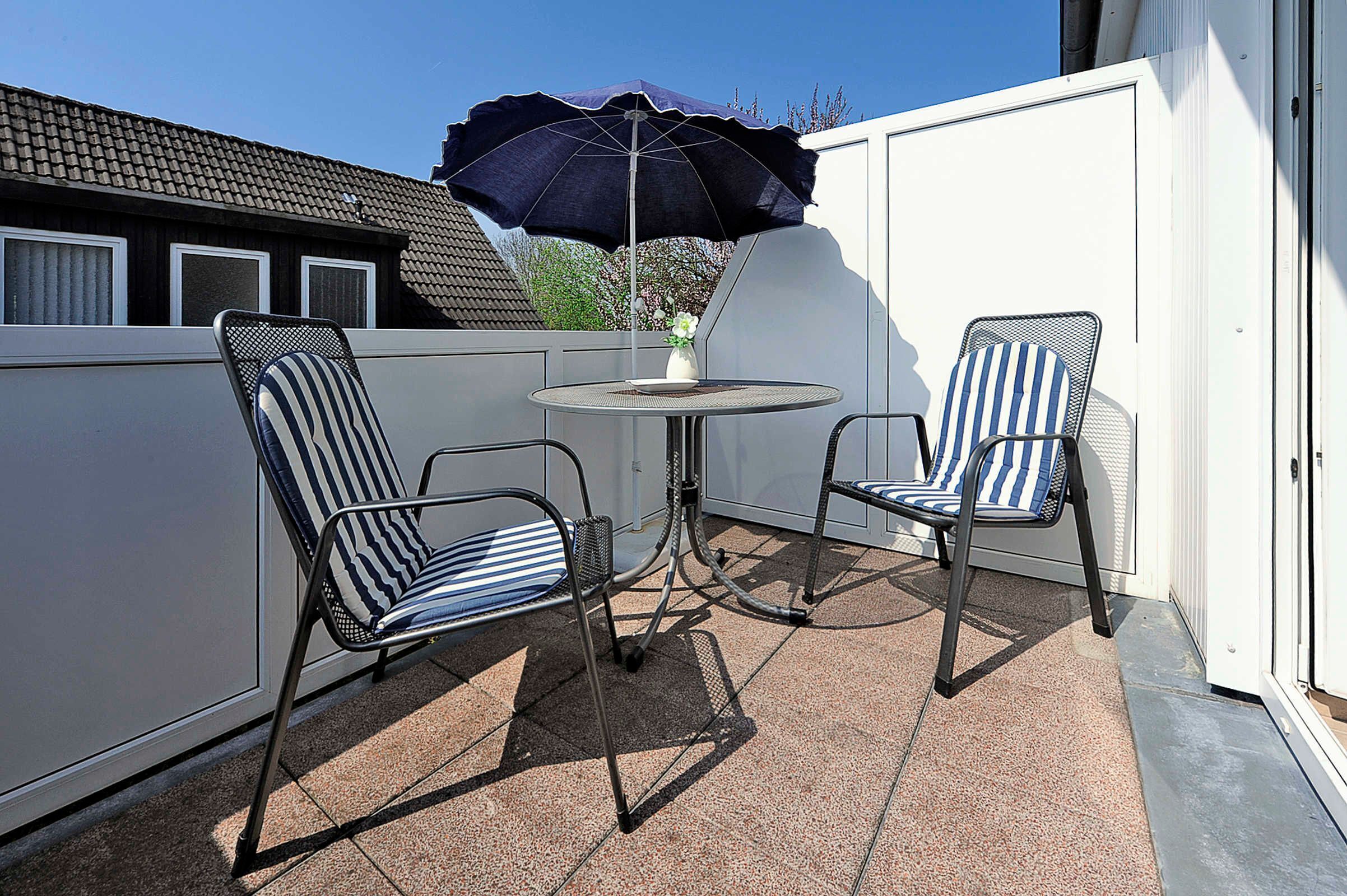 Een terras met twee gestreepte stoelen, een tafel, een parasol en een witte hek.