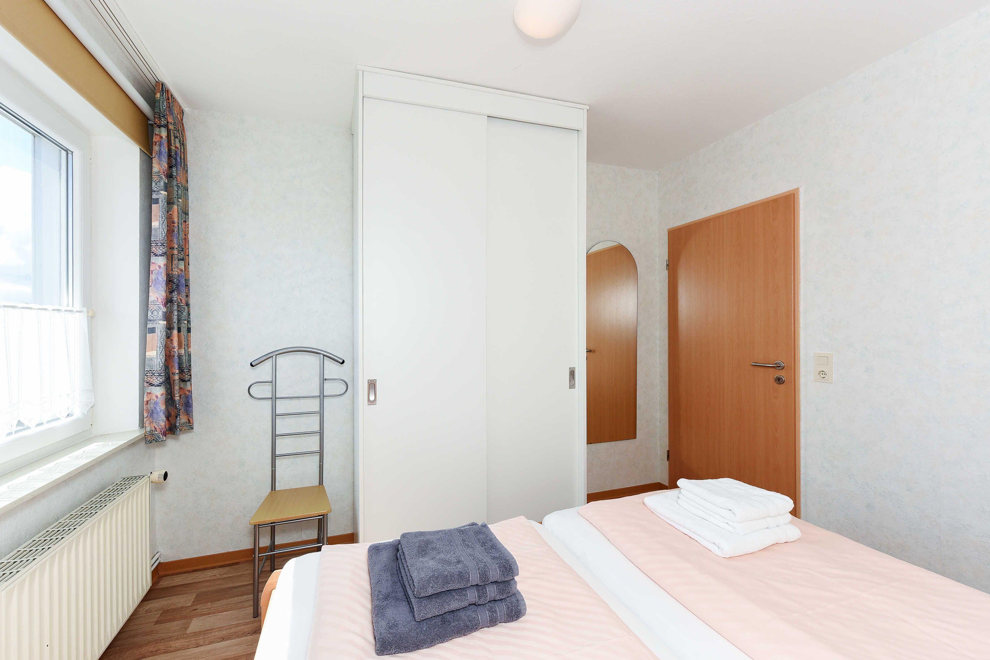 A bedroom with a bed, a chair, a radiator, and a window with curtains.