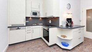 Une cuisine moderne avec des meubles blancs, un four à micro-ondes encastré, une machine à café et une horloge murale.