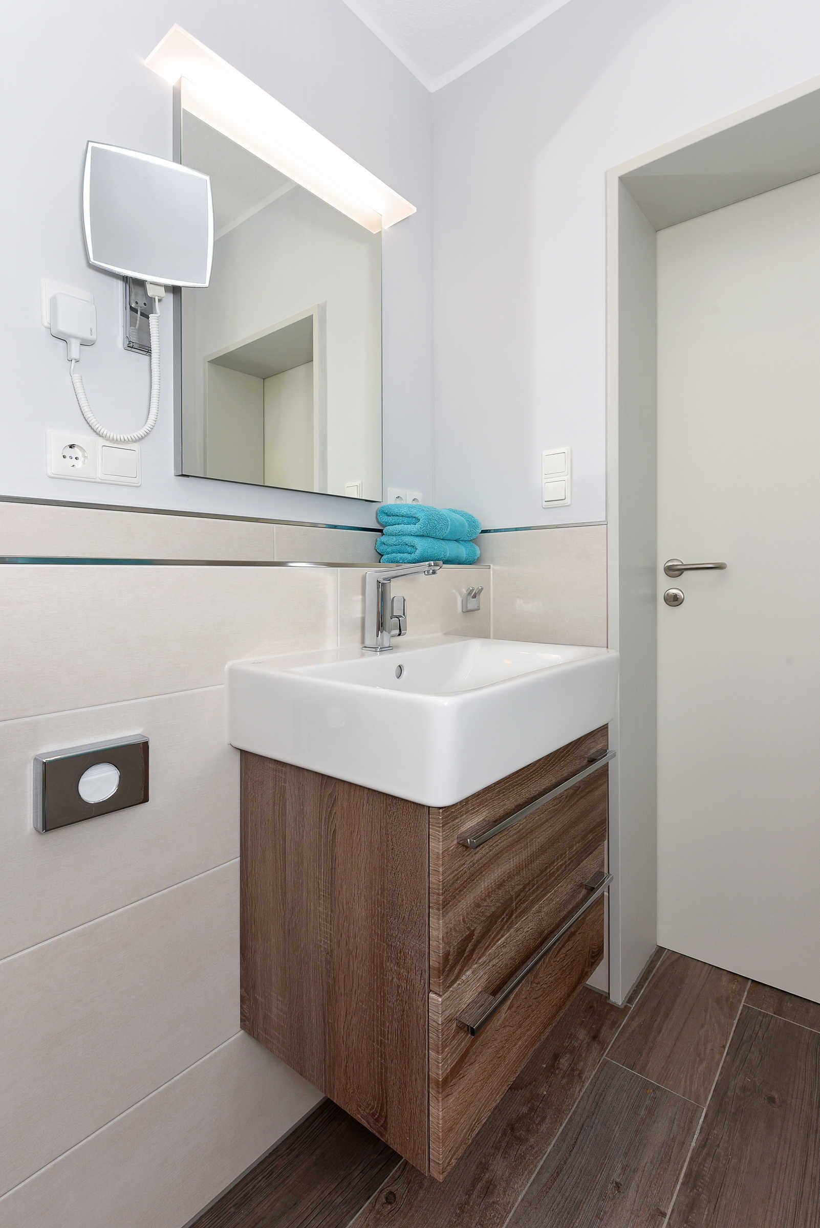 A modern bathroom with a white sink, wooden vanity, and a mirror with integrated lighting.