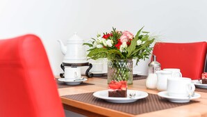 Une table à manger avec une théière blanche, un vase rempli de fleurs et une part de gâteau sur une assiette.