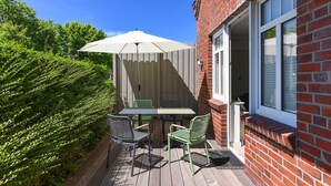 Une terrasse avec une table et des chaises, un parasol blanc et un mur en briques.