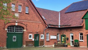 Un bâtiment en briques rouges, avec une porte et des fenêtres vertes, des panneaux solaires sur le toit et une enseigne indiquant « Pittlacherhof ».