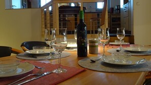 Une table à manger dressée avec des verres à vin, des assiettes et des couverts, et une bouteille de vin placée au centre.
