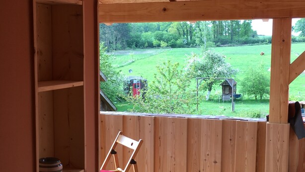 Une pièce en bois donnant sur un champ verdoyant et une structure rouge.