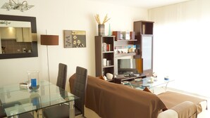Una sala de estar moderna con una mesa de comedor de vidrio, sillas de cuero, un sofá, una estantería, un televisor de pantalla plana y un jarrón decorativo.
