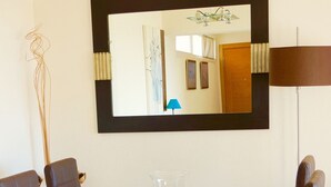 Un área de comedor moderna con una mesa de vidrio, cuatro sillas y un espejo grande en la pared.