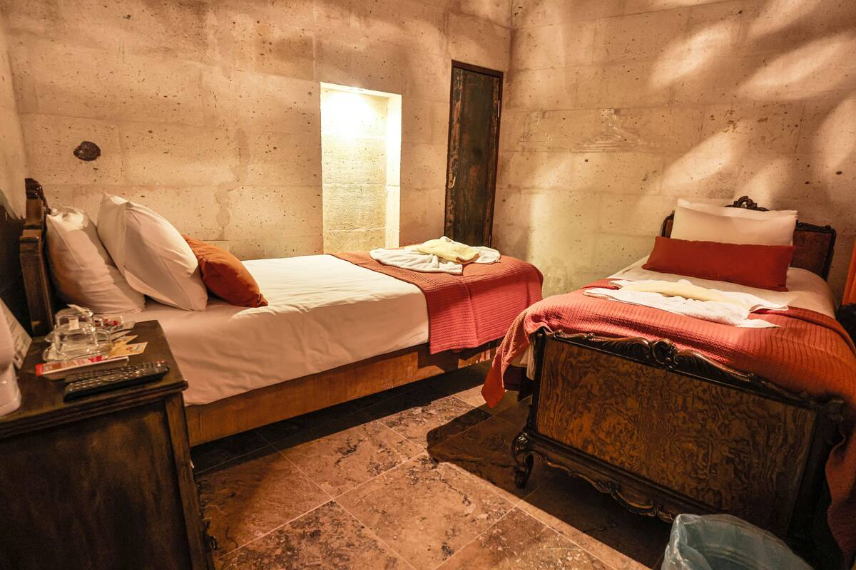 A small, dimly lit room with two beds, a wooden dresser, and a window.