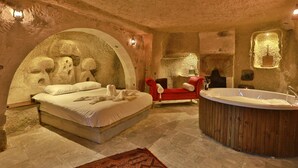 Una habitación con pared de piedra, una cama, un sofá rojo y una bañera de madera.
