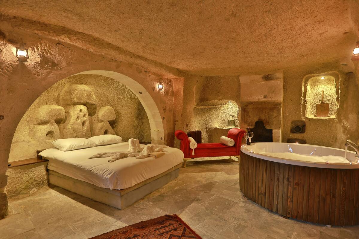 A room with a stone wall, a bed, a red sofa, and a wooden bathtub.