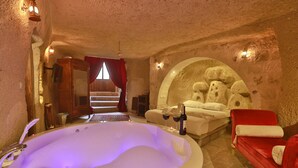 Un cuarto de spa con una bañera grande, un sofá rojo y una pared de piedra.