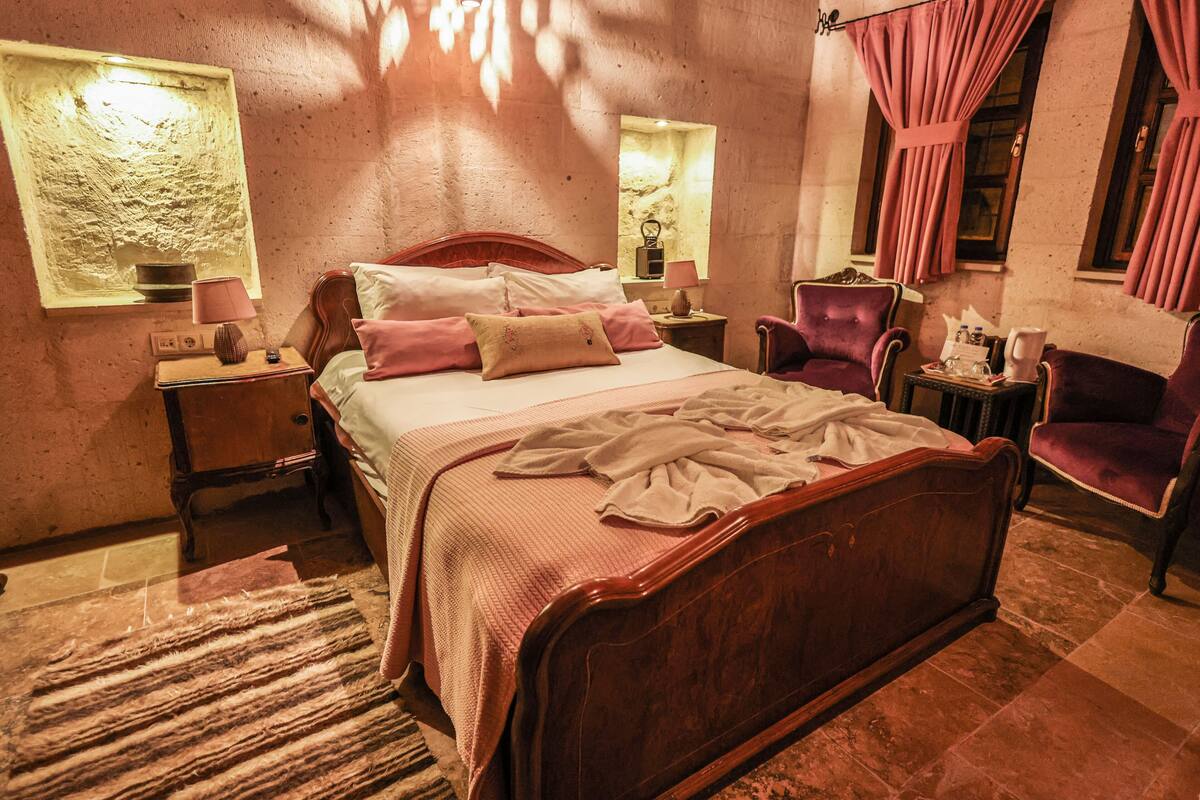 A bedroom with a wooden bed, a nightstand, a chair, and a window with curtains.
