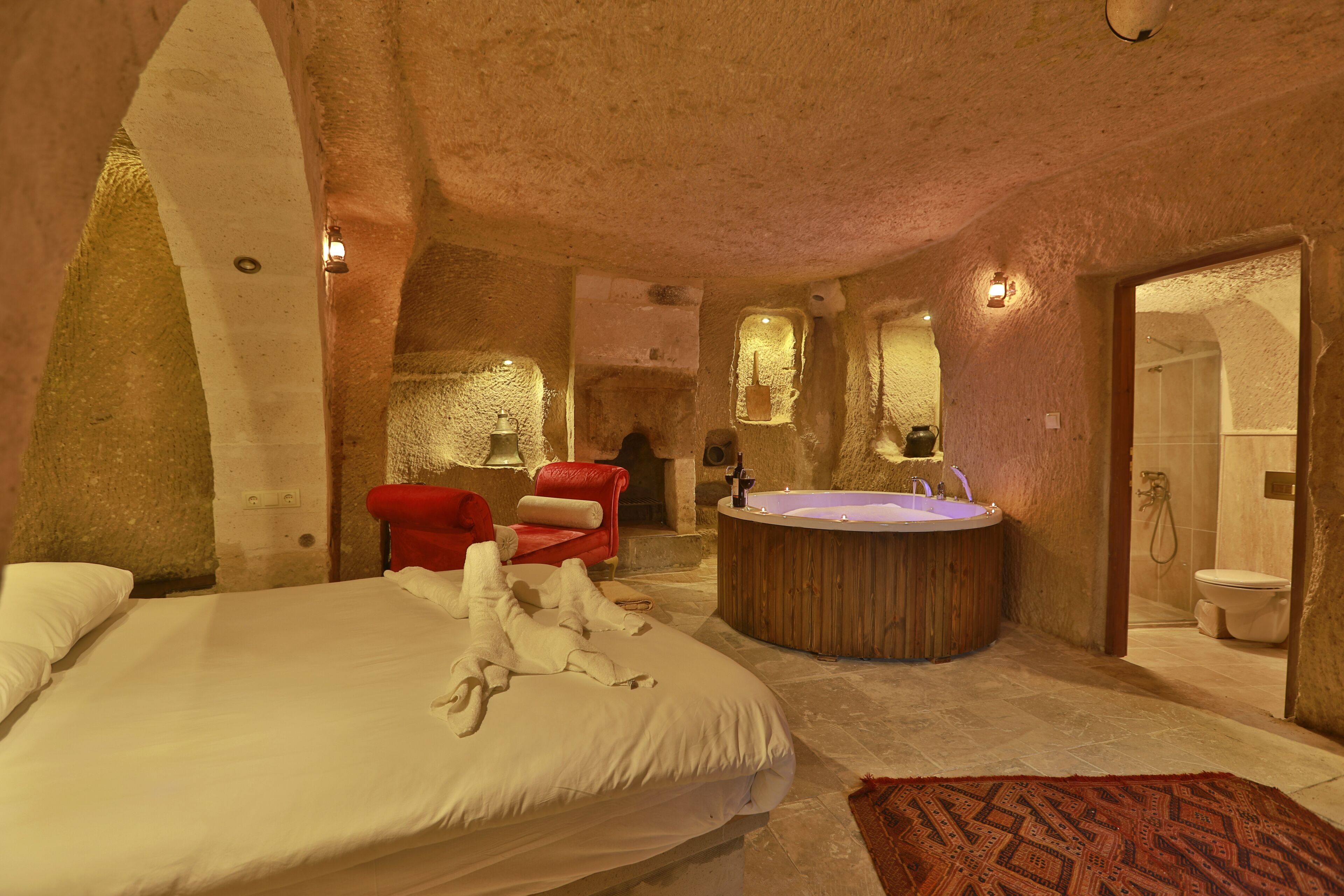 Una habitación amplia con una cama grande, una silla roja, una bañera de madera y zona de ducha.