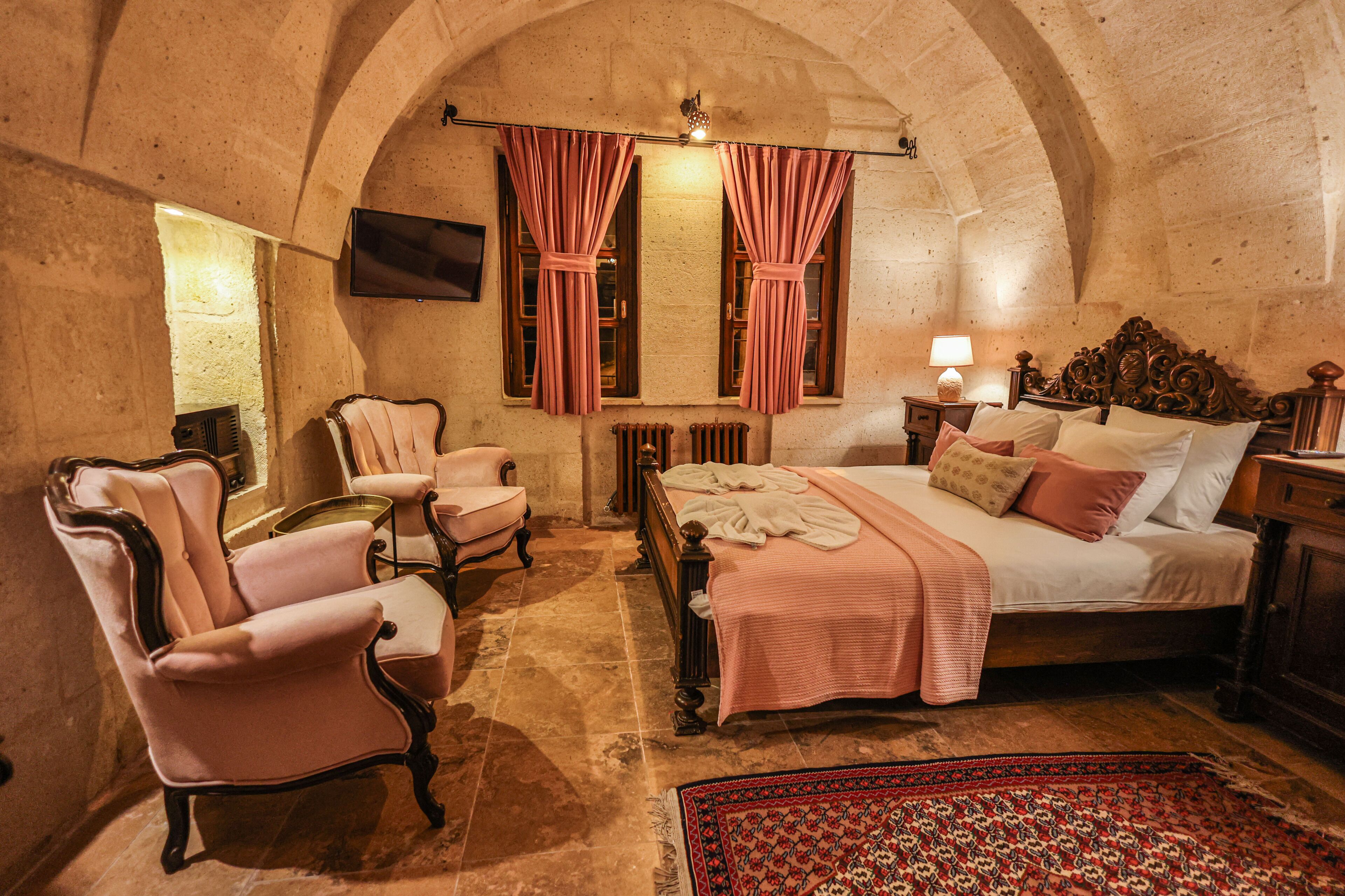 A bedroom with a bed, two chairs, a TV, and a patterned rug.