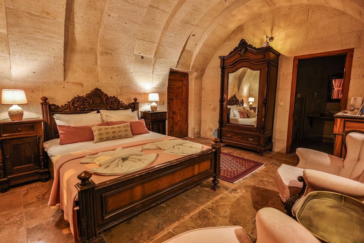 A bedroom with a large bed, wooden headboard, two bedside tables with lamps, a large mirror, and a chair.