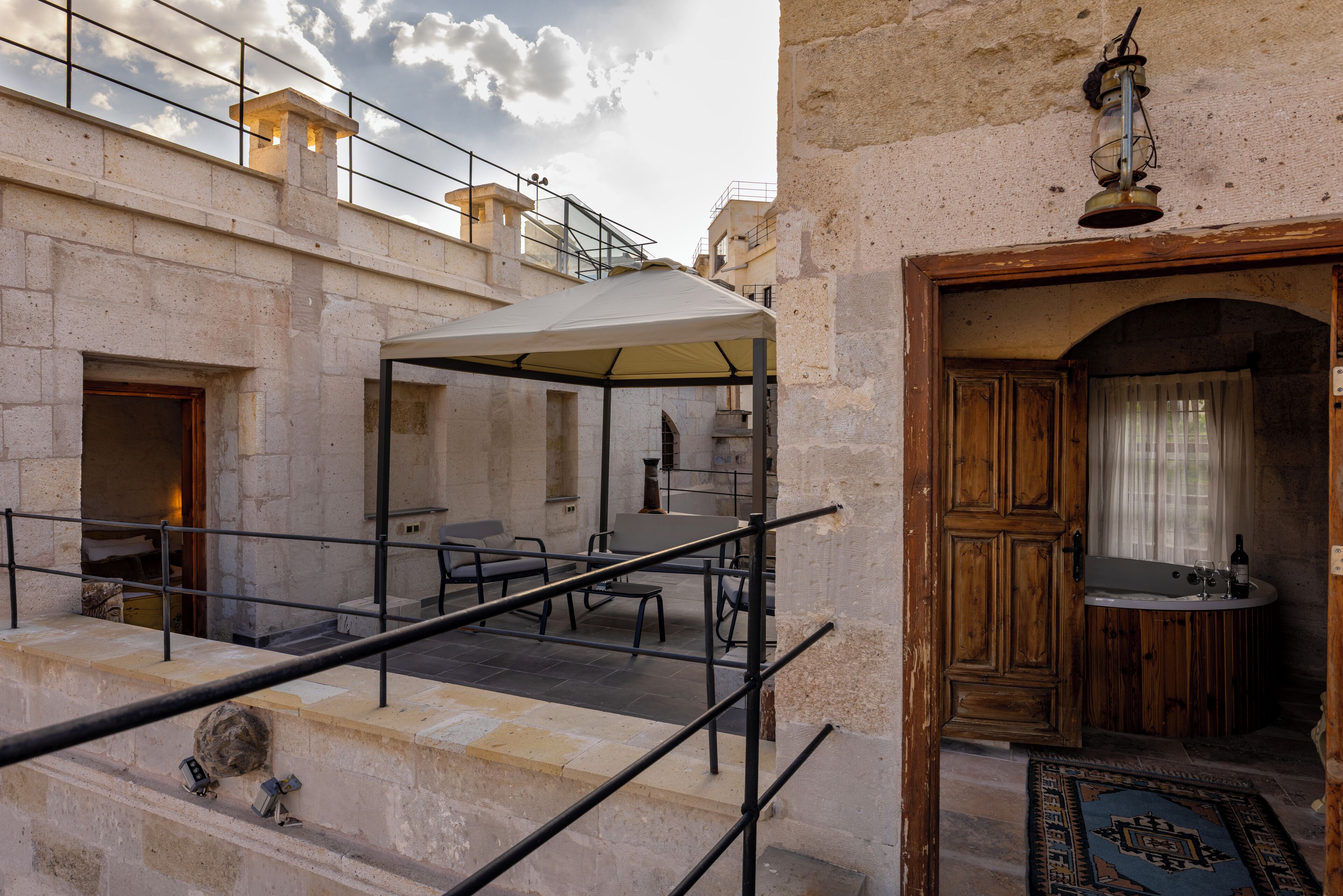 Un edificio de piedra con una zona de estar al aire libre techada, una puerta de madera y un baño pequeño con lavabo y espejo.