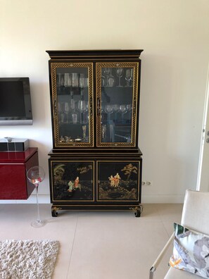 Ein Zimmer mit einem schwarzen Schrank mit Glastüren, einem roten Nachttisch, einem Weinglas und einem Kissen mit Blumenmuster.