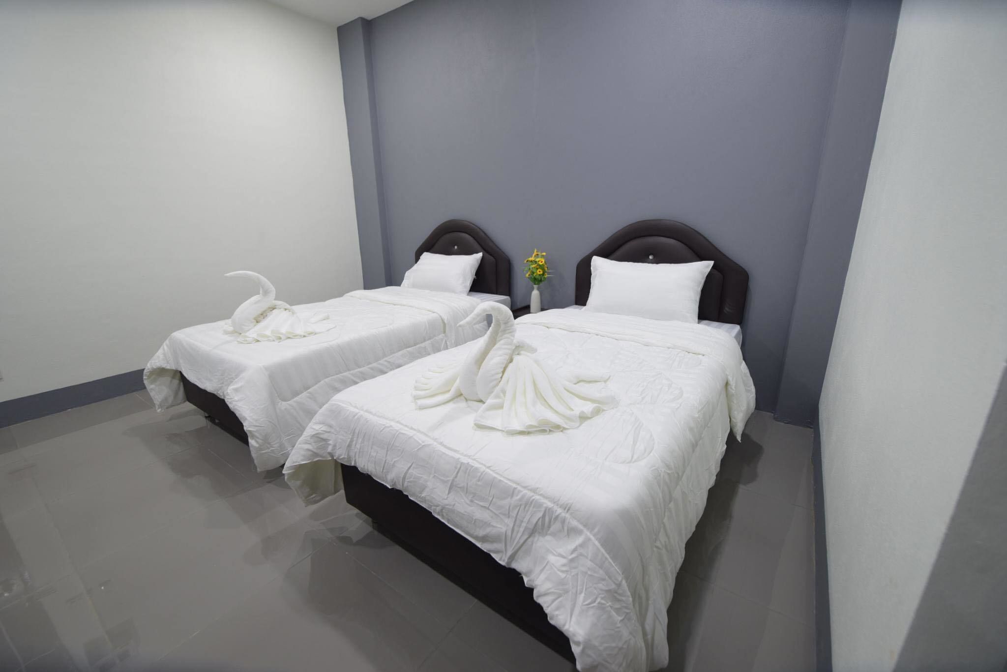 Habitación de hotel con dos camas, cada una con una colcha blanca y una toalla decorativa con forma de cisne.