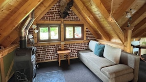 A cozy attic room with a brick wall, wooden beams, a sofa, a table, and a wood stove. - Vacation in the Ore Mountains (Sehmatal-Cranzahl)