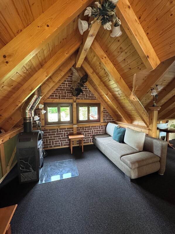 A cozy attic room with a brick wall, wooden beams, a sofa, a table, and a wood stove. - Vacation in the Ore Mountains (Sehmatal-Cranzahl)