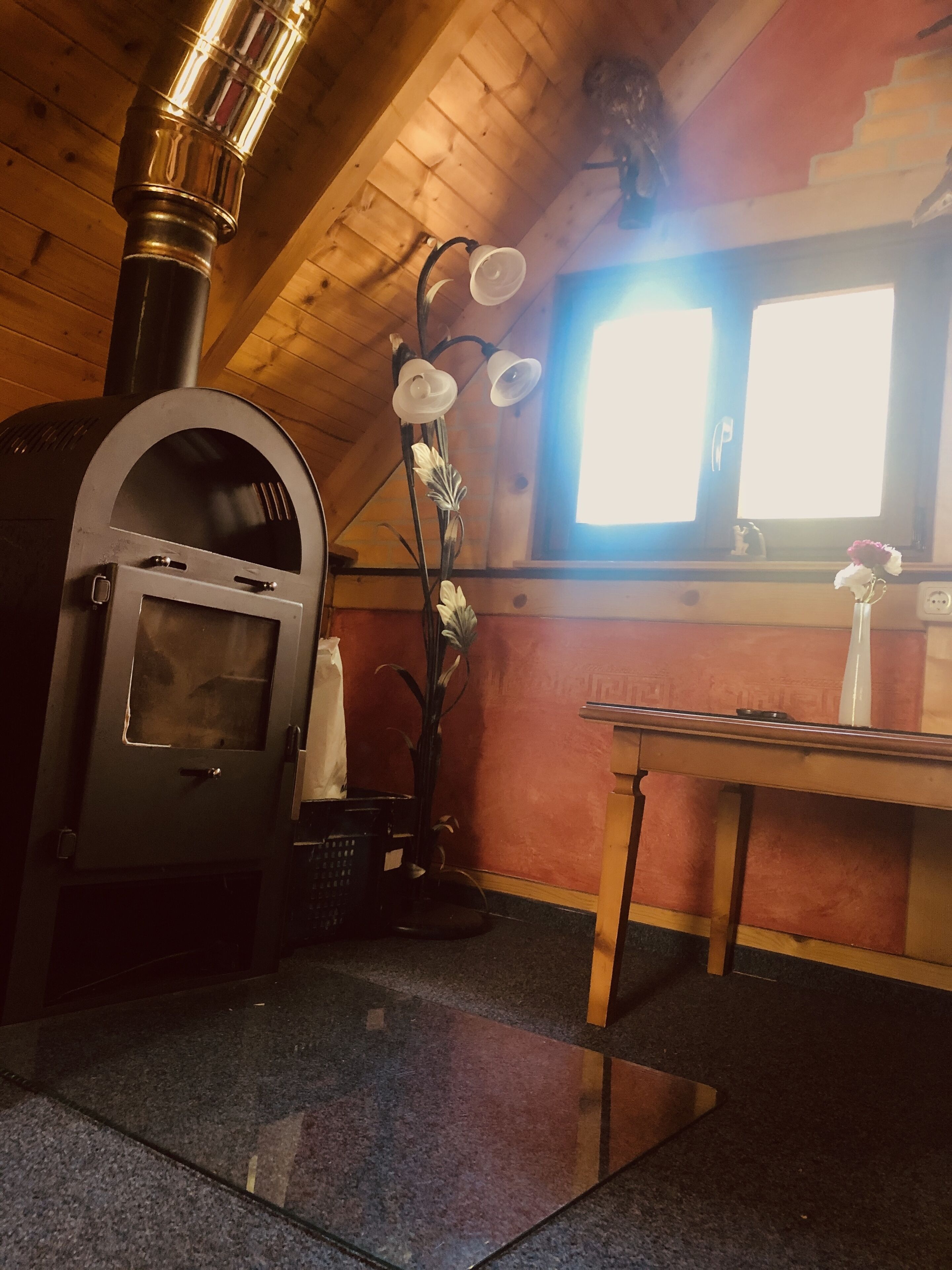 A kitchen with a wood-burning stove, a window, and a vase with flowers on a table.