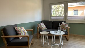 A room with a sofa and two chairs, a small table, and a window with a view of trees and buildings. - Vacation home close to nature with fireplace and rowing boat on Lake Plau - House 26 (Plau am See OT Quetzin)