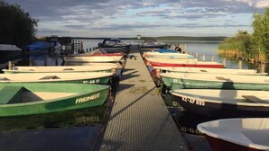 A dock with several boats moored in a row, a wooden walkway leading to the water, and a calm lake in the background. - Vacation home close to nature with fireplace and rowing boat on Lake Plau - House 26 (Plau am See OT Quetzin)
