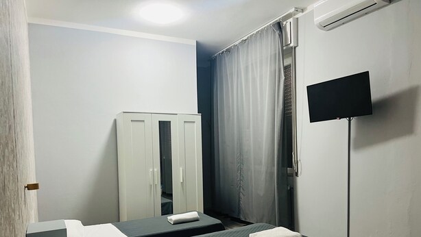 A hotel room with two beds, a wardrobe, a TV, and a shower curtain. - Il Galileo Rooms (Pisa)