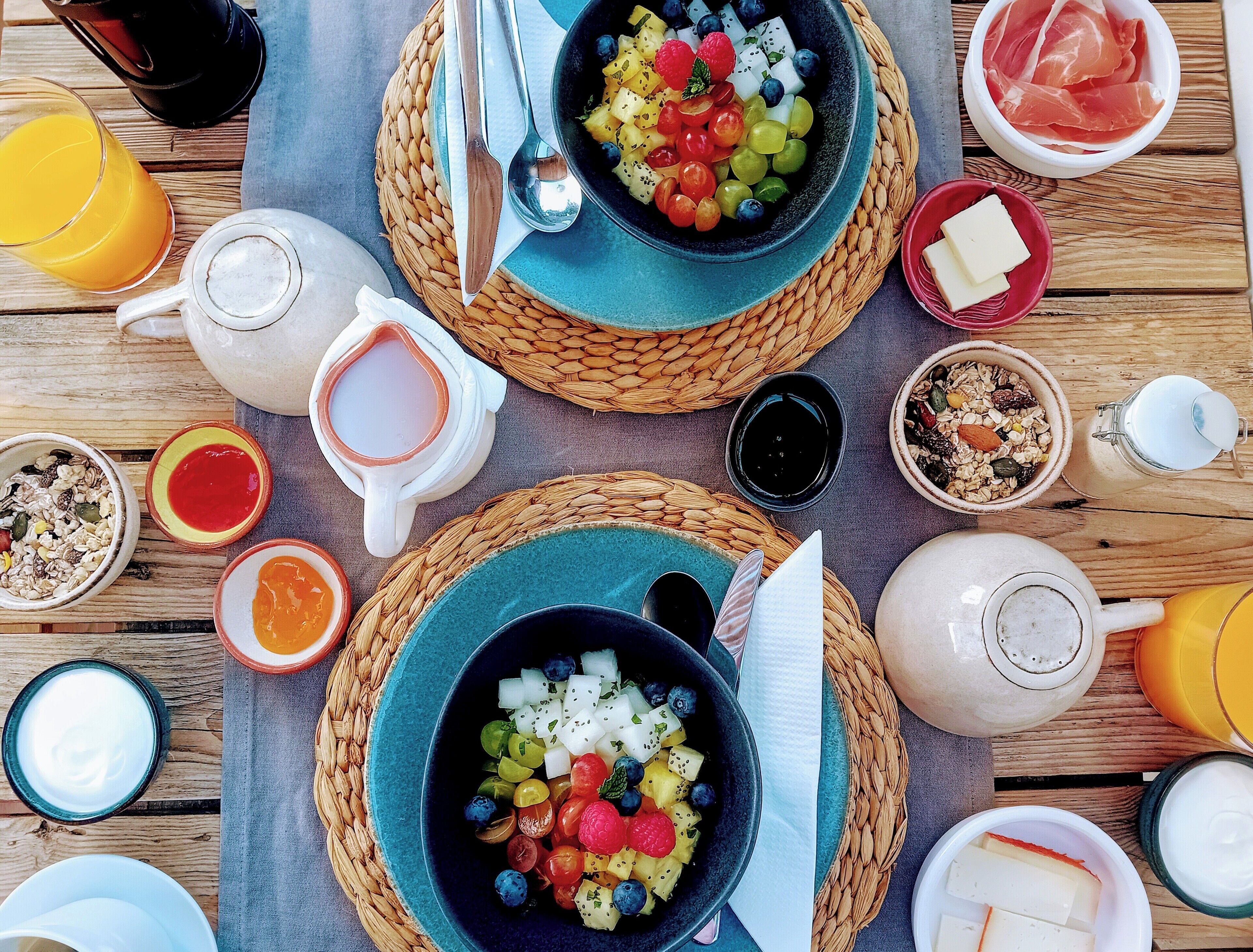 Une table en bois dressée pour le petit-déjeuner, avec divers aliments et boissons.