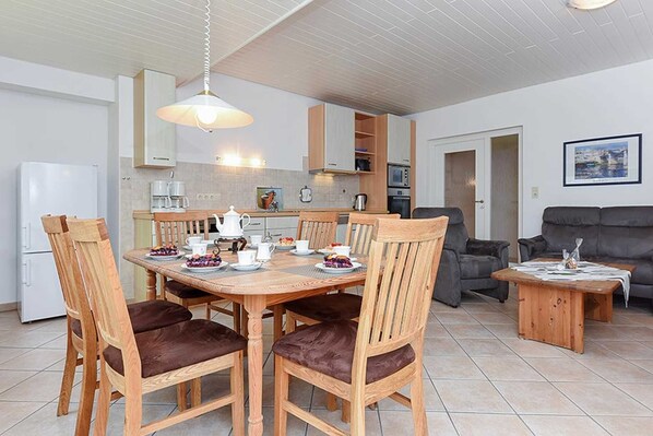 A modern kitchen with wooden cabinets, a dining table set for four, and a grey sofa in the living area.