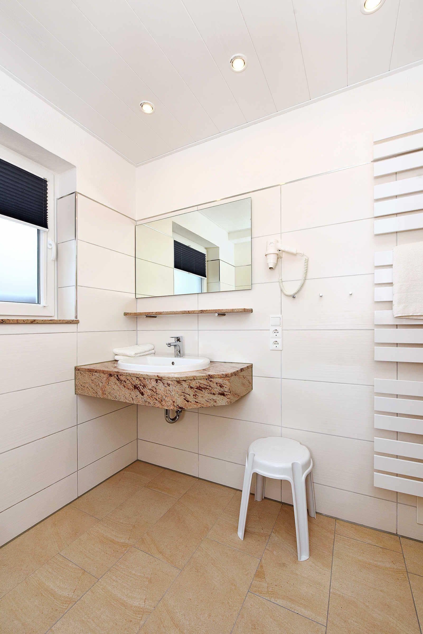 A modern bathroom with a marble sink, a large mirror, a hairdryer, and a white stool.