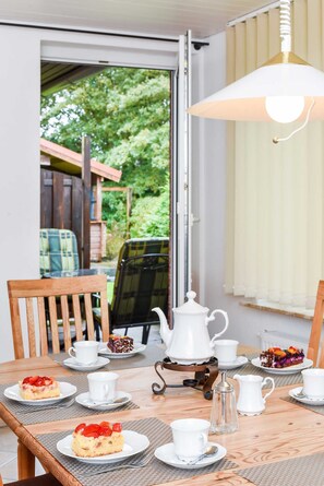 A dining table set with white cups, saucers, and plates with food, a white teapot, and a sugar bowl.