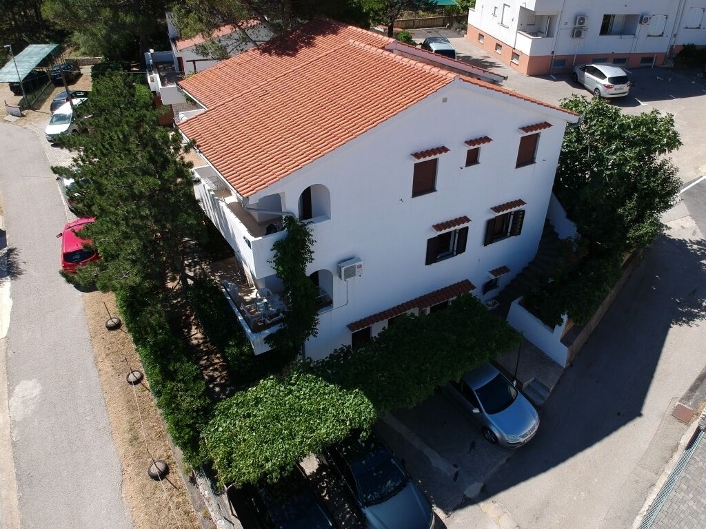 Un edificio blanco con techo de tejas rojas, numerosas ventanas y un estacionamiento con coches.