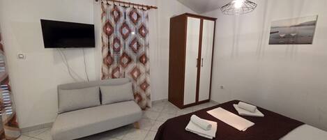 A bedroom with a bed, a sofa, a wardrobe, a TV, and a painting on the wall.