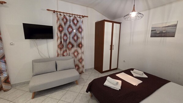 A bedroom with a bed, a sofa, a wardrobe, a TV, and a painting on the wall.