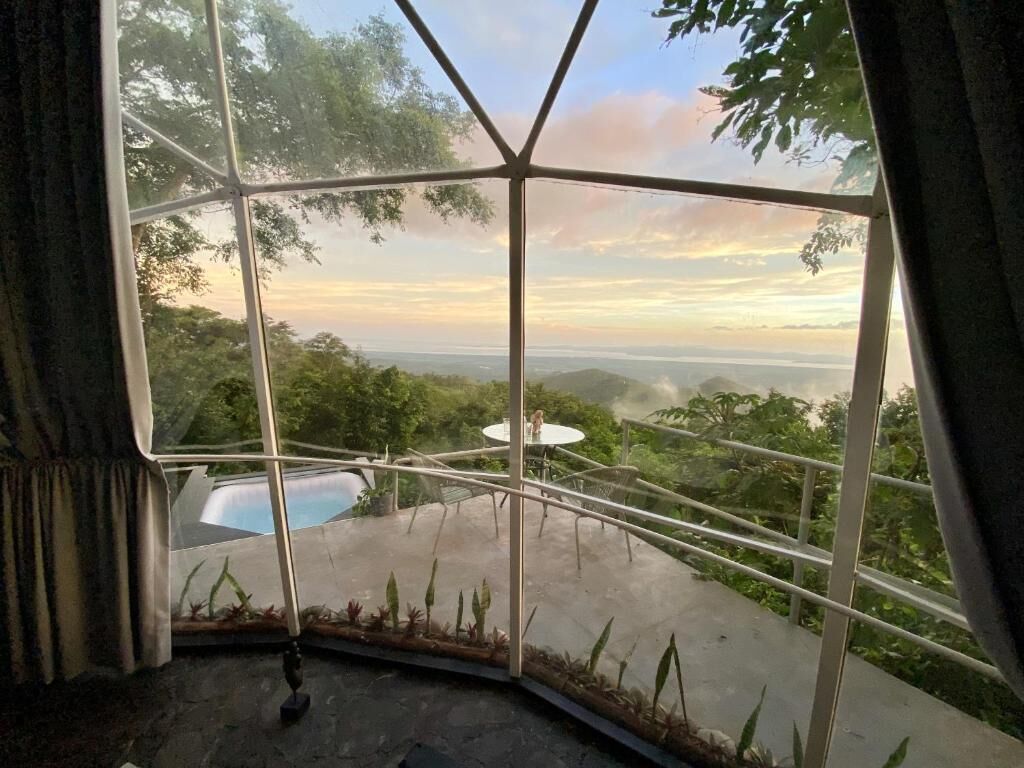 A room with a large window offering a view of a pool and surrounding greenery.